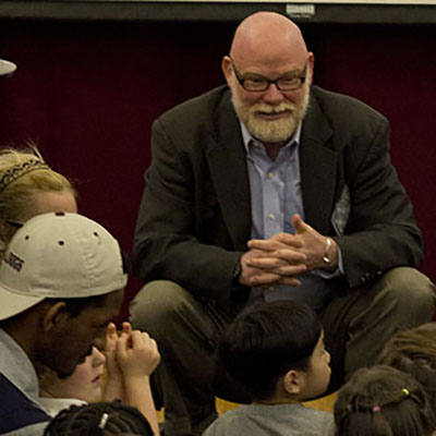 Students gathered around a lecturer sitting on the floor.