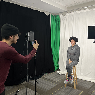 A student takes a photograph of a fellow student in the Photography Studio.