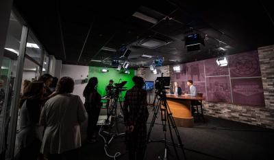 A production crew in a television studio work with students at the anchor desk.