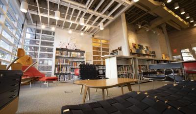 Seating area with bookshelves in front of large picture windows with a view of the street outside.