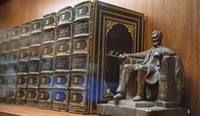 A small statue of Abraham Lincoln sits on a shelves with volumes of books.